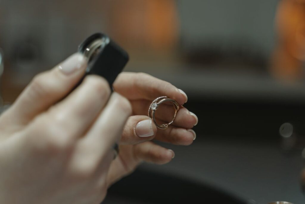 Hands holding a ring up beside a black jeweller's loupe